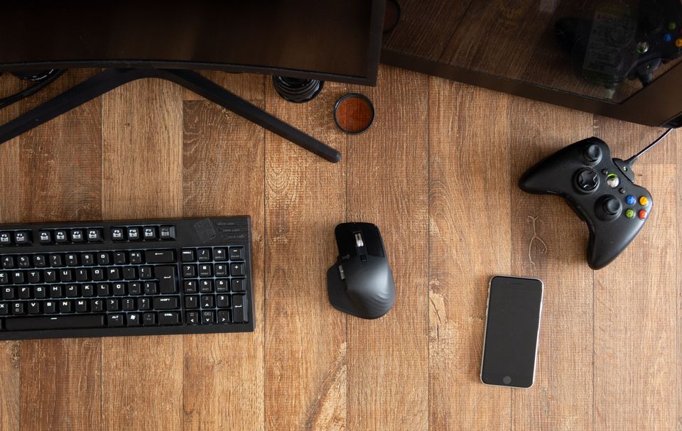 Een bureau van bovenaf gezien met toetsenbord, muis, smartphone en gamecontroller